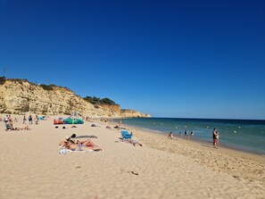A beach with people sunbathing and swimming, a green car, and a flag.