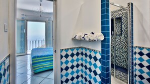 A bathroom with blue and white checkered tiles, a towel rack with rolled towels, and a glass shower enclosure. - DOMUS VIGNA Fusco, AMALFI COAST (FURORE (SA))