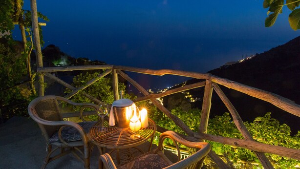 A wicker chair and table with candles, overlooking a coastal view at night. - DOMUS VIGNA Fusco, AMALFI COAST (FURORE (SA))