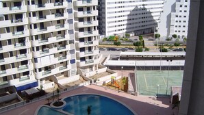 Un edificio residencial con varios balcones, piscina y cancha de tenis.