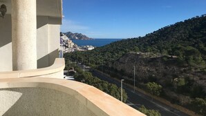 Un balcón con vistas a un pueblo costero, una carretera y un paisaje montañoso.