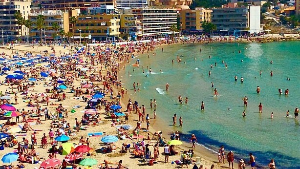 Una playa concurrida, con muchos sombrillas y gente disfrutando del agua.