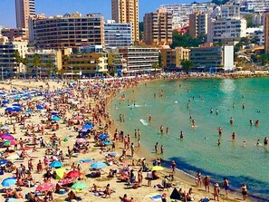 Een druk strand met veel parasols en mensen die van het water genieten.