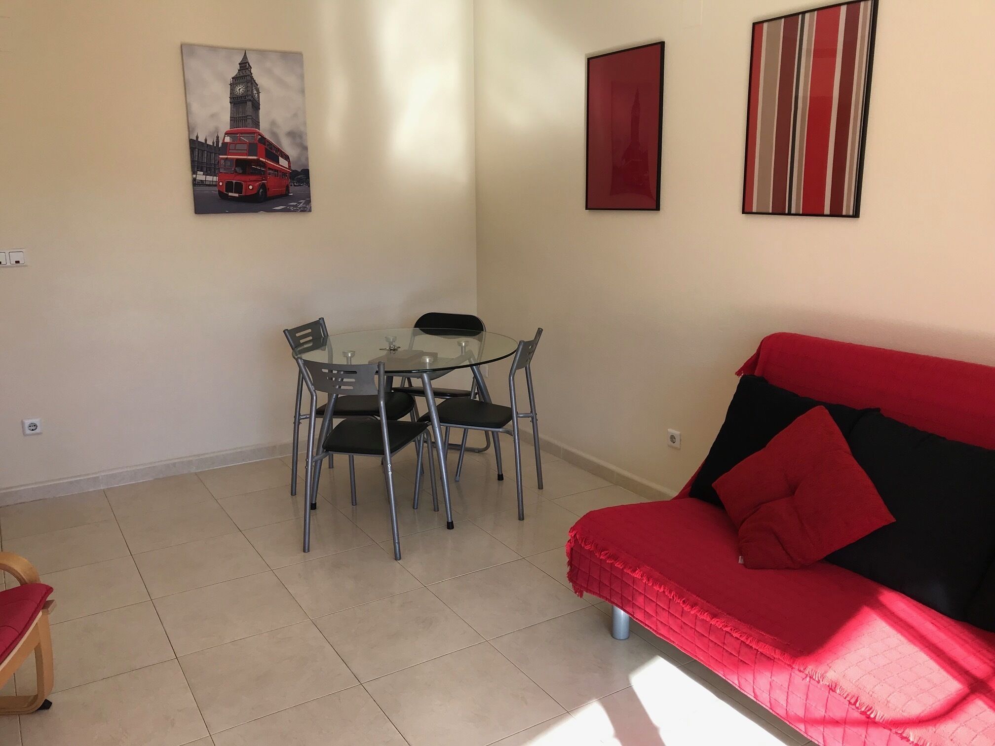 A living room with a red sofa, a glass dining table with four chairs, and two framed pictures on the wall.