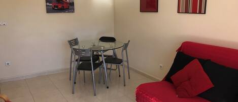 A living room with a red sofa, a glass dining table with four chairs, and two framed pictures on the wall.