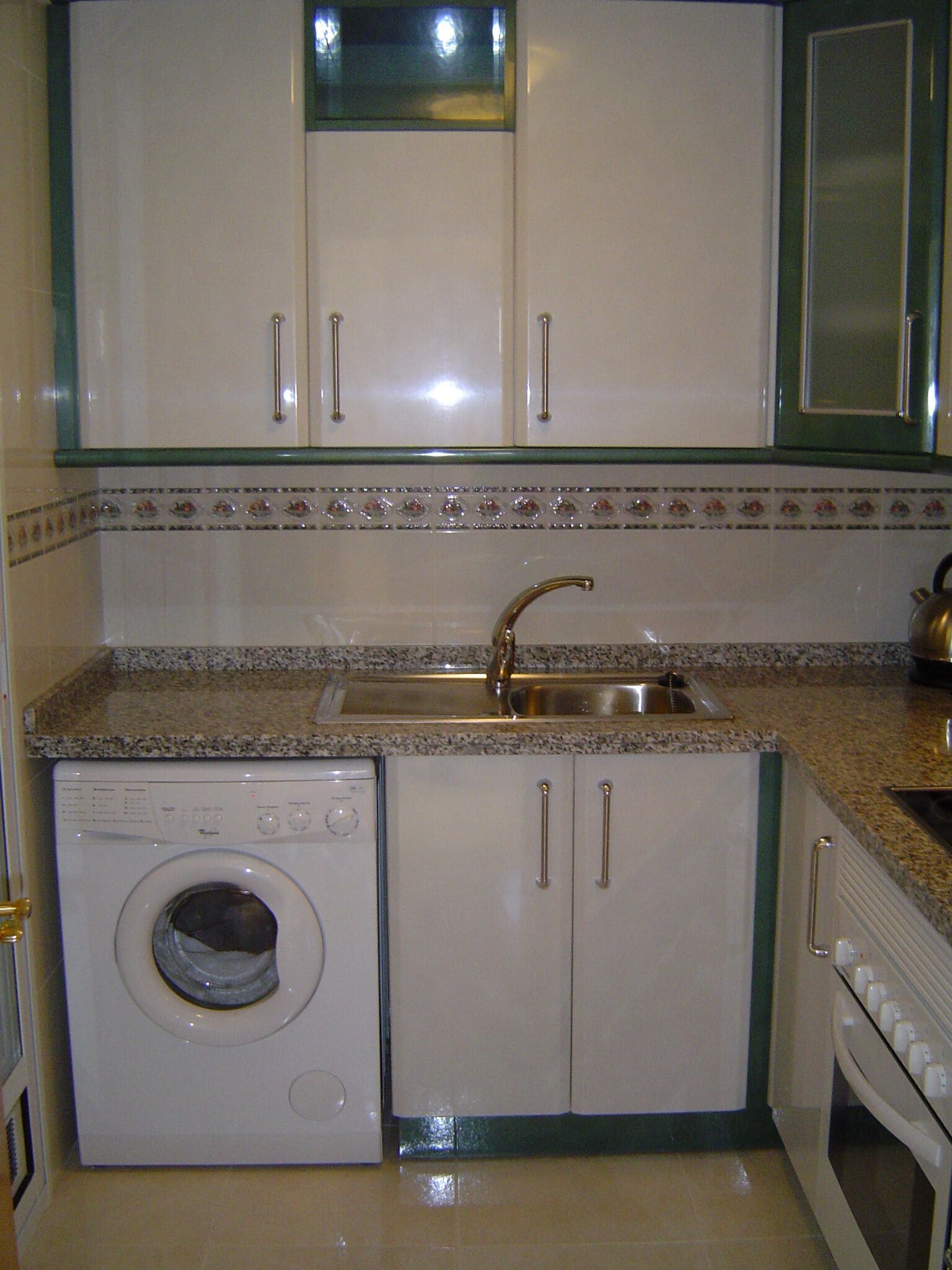 A compact kitchen with a built-in washer and dryer, a stainless steel sink, and a granite countertop.