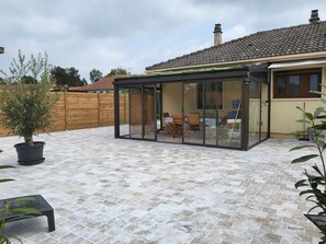 Ein überdachter Patio-Bereich mit Glasveranda, Esstisch und Stühlen.