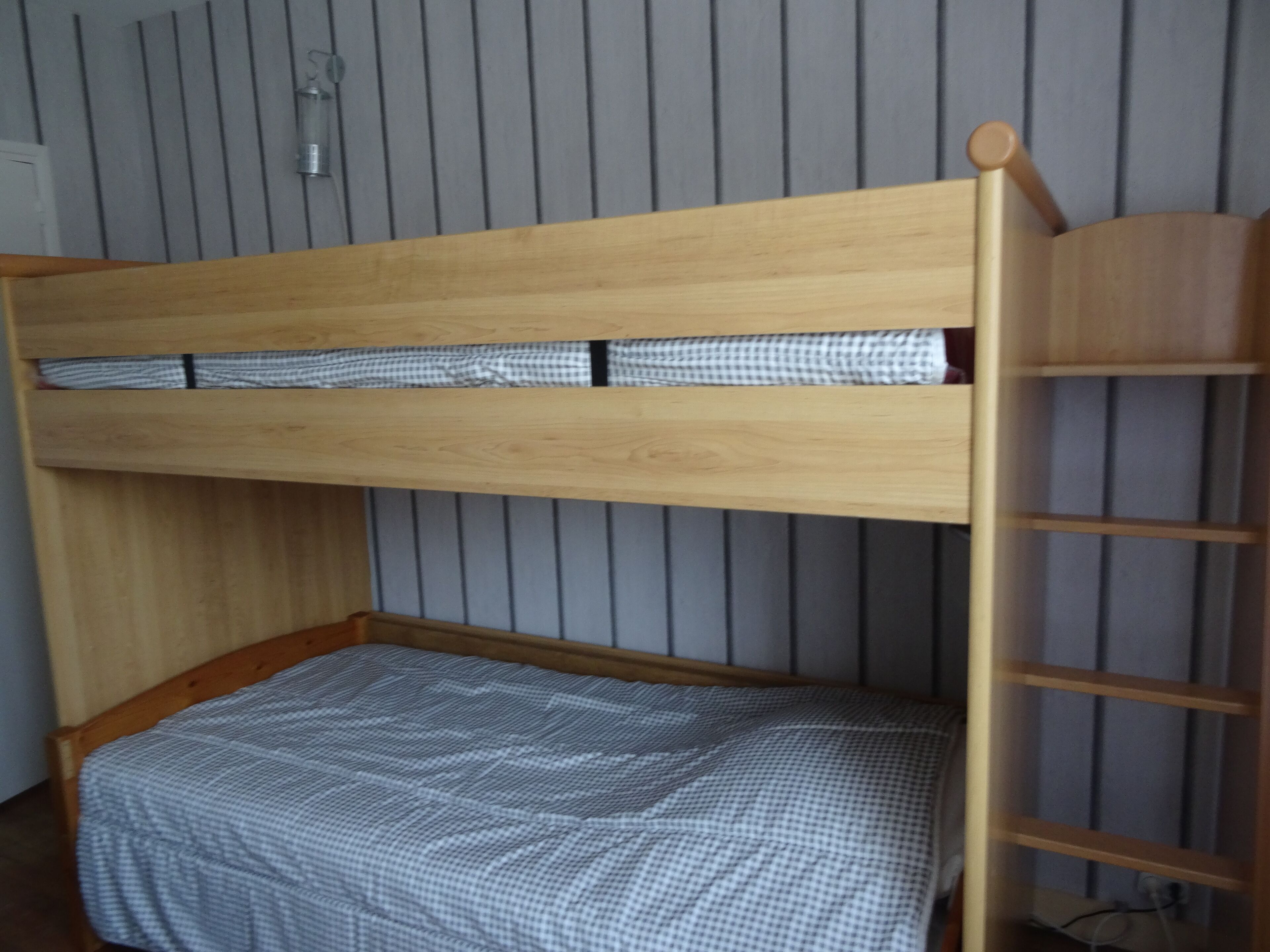Ein Stockbett mit Holzrahmen und karierter Bettdecke.