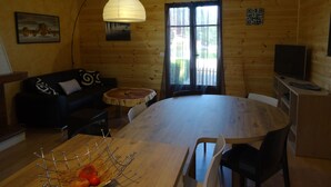 A cozy cabin interior with a wooden dining table, a black sofa with patterned cushions, a round wooden table, and a television on a wooden stand. - In Mimizan-plage sud, detached house with fenced garden, 2km from beaches (Mimizan)