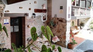 Un edificio de piedra con puerta de madera, balcón con barandilla y plantas en macetas.