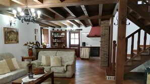 Una sala de estar acogedora con sofá, mesa de centro y chimenea. Una escalera conduce a un nivel superior.