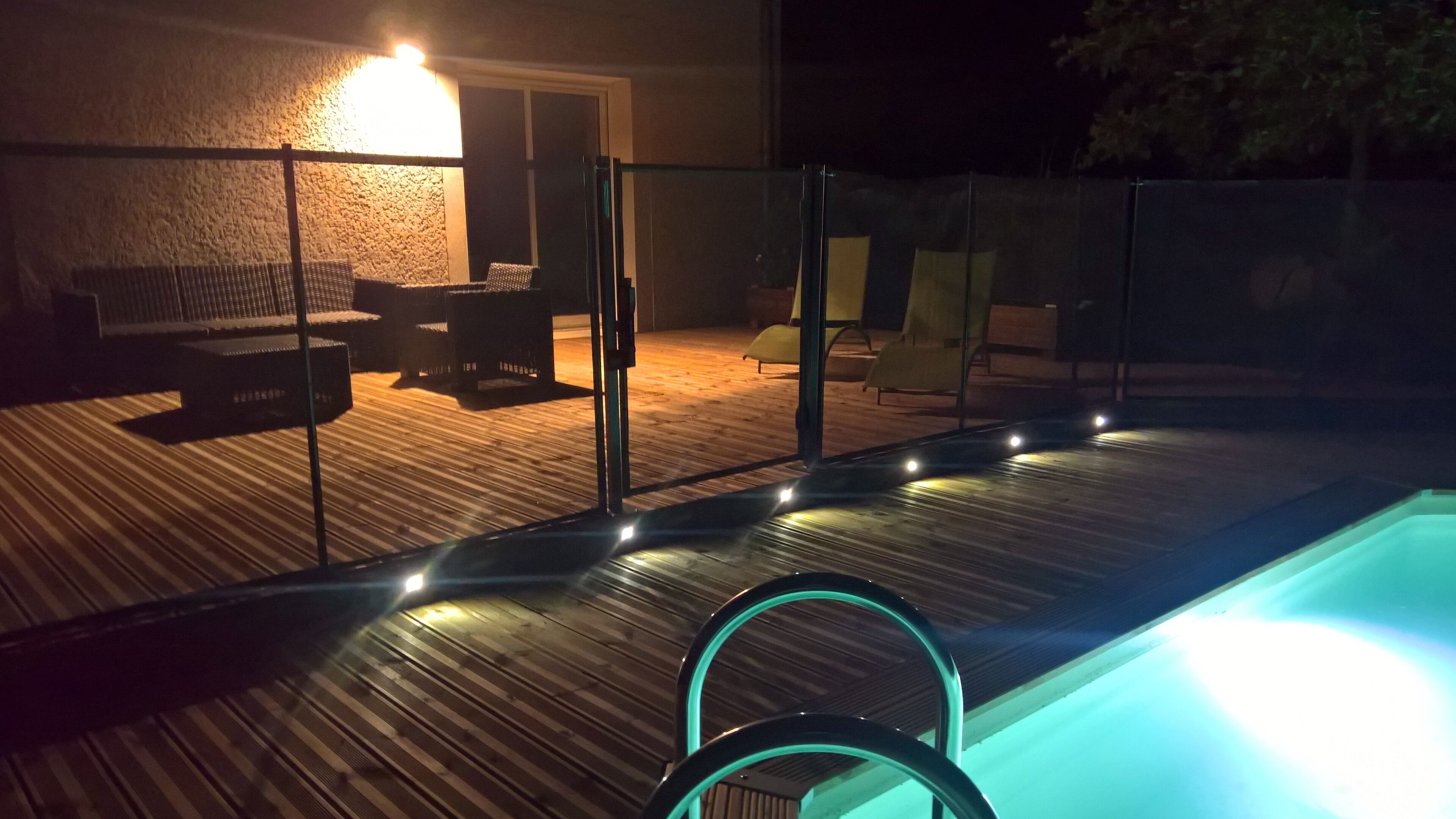 Un espace piscine doté d’une terrasse en bois, d’une clôture en verre et de mobilier d’extérieur.