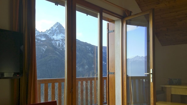 Une pièce dotée d’une grande porte-fenêtre coulissante donnant sur un balcon avec vue sur les montagnes.