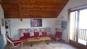Un salon chaleureux avec un plafond en bois, un canapé à carreaux rouges et blancs, une table en bois et un fauteuil rouge.
