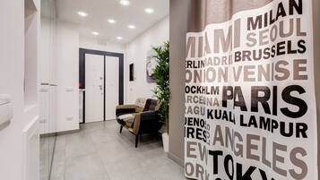 Un hall d’hôtel moderne comprenant un comptoir d’accueil, un espace salon avec un fauteuil et un mur sur lequel sont inscrits des noms de villes.