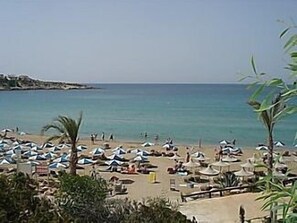 A beach with numerous umbrellas and sun loungers, a clear sky, and calm sea.