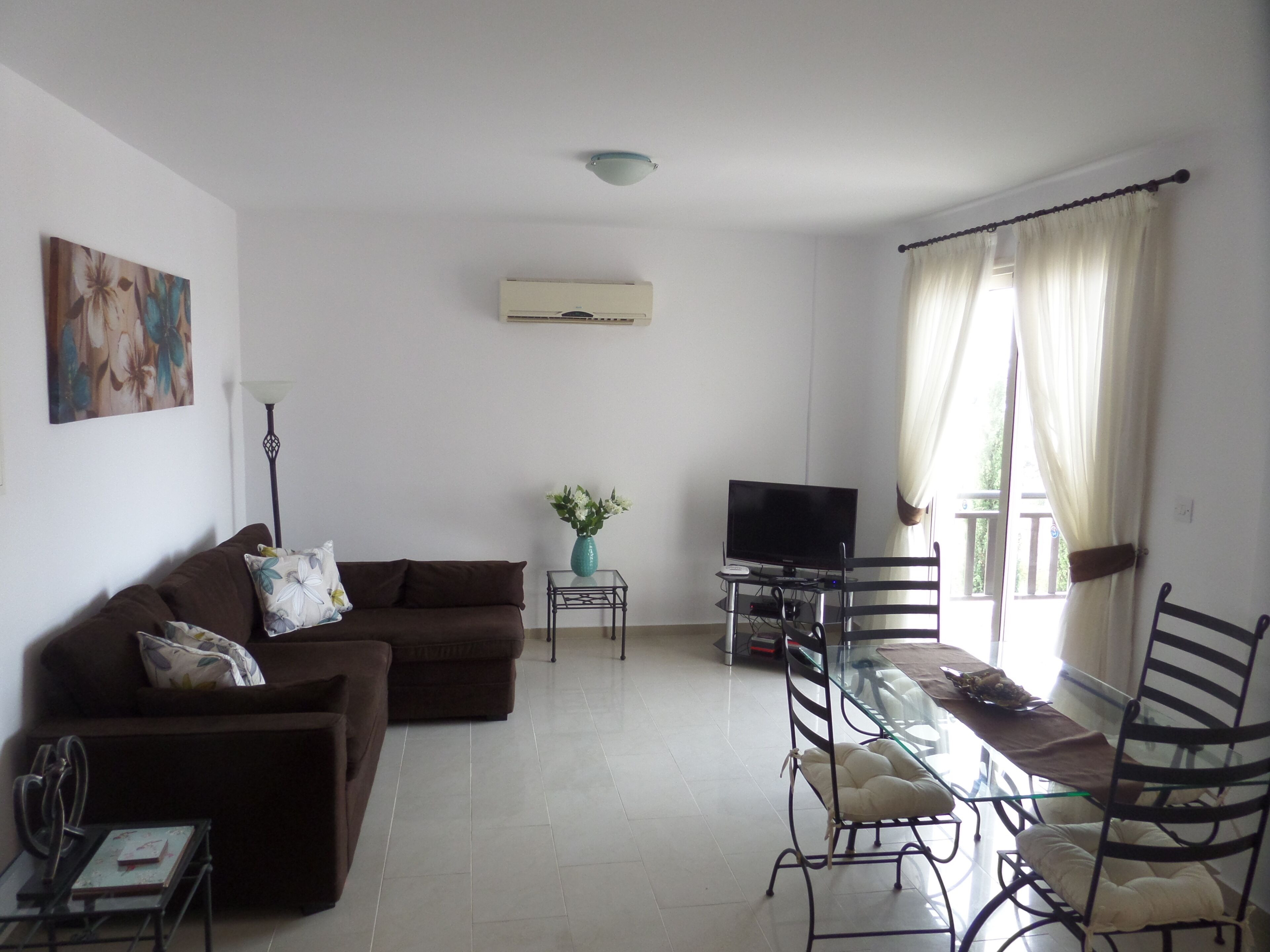 Uma sala de estar com um sofá, uma televisão, uma mesa de vidro e uma cadeira.