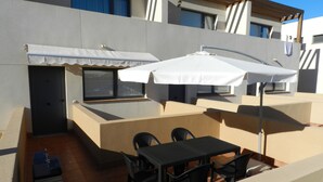 Een terras op het dak met een tafel en stoelen, een barbecue, en een overdekt gebied met parasols.