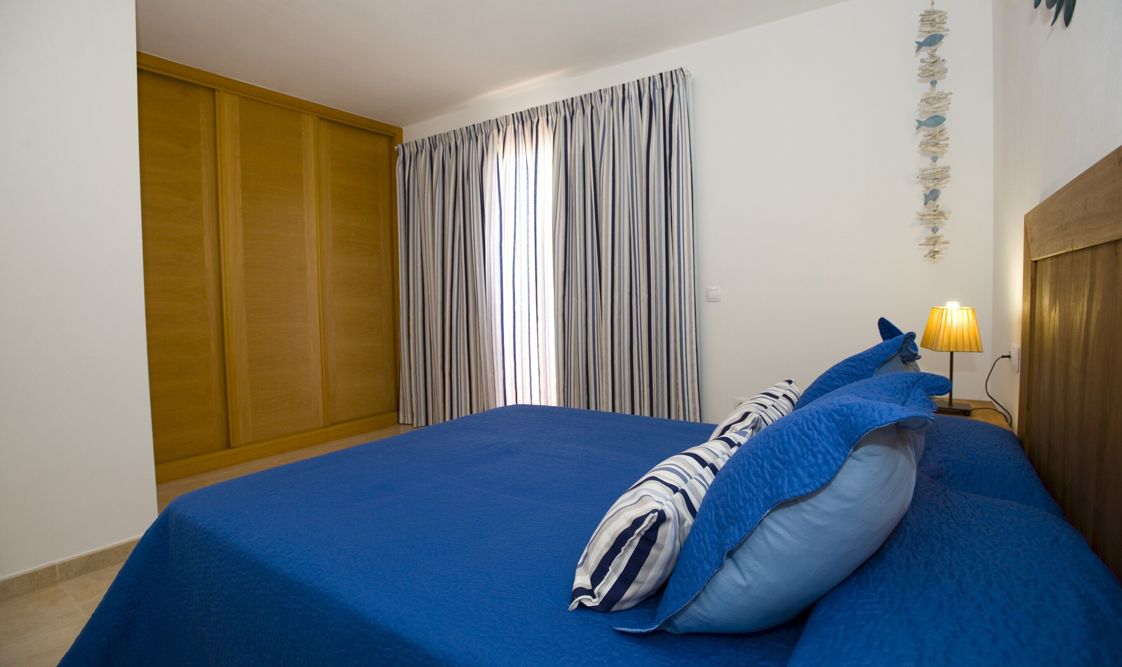 Un dormitorio con cama, mesita de noche, lámpara, cortina y armario de madera.