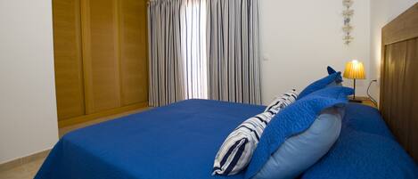 Un dormitorio con cama, mesita de noche, lámpara, cortina y armario de madera.
