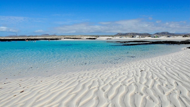 Een strand met helder turquoise water en wit zand.