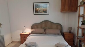 A bedroom with a bed, two nightstands, a radiator, a wooden cabinet, and a bookshelf.