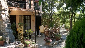 A stone building with a balcony, outdoor seating area with chairs and tables, and potted plants.
