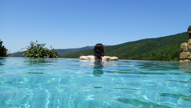 Una persona en una piscina cristalina con un paisaje montañoso al fondo.