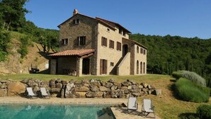 Una casa de piedra con piscina y sillones de descanso.