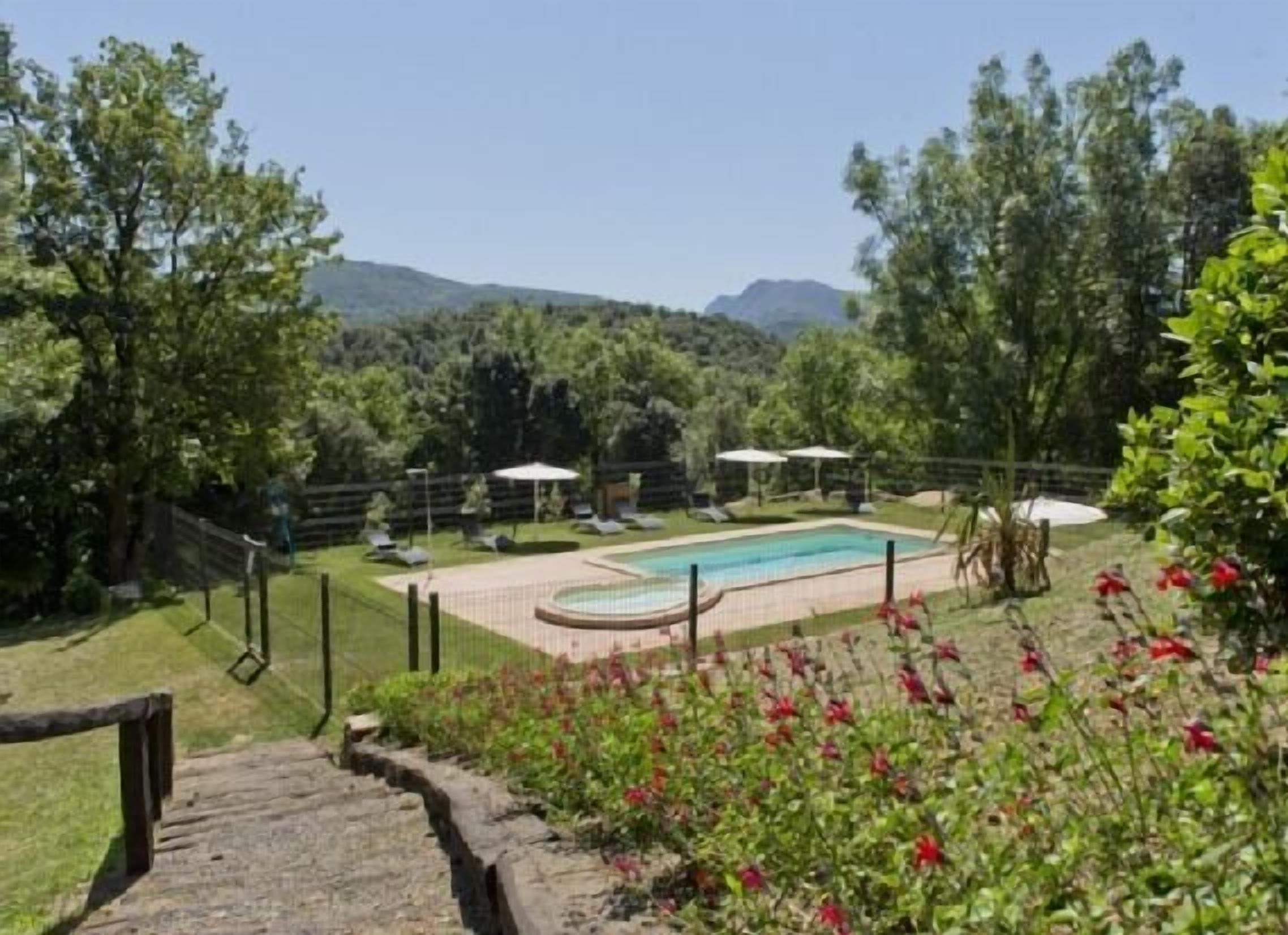 Un espace piscine offrant une vue sur les montagnes, entouré d’arbres et délimité par une clôture en bois.