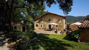 Une maison en pierre avec un toit en tuiles, entourée d’un jardin bien entretenu et d’arbres.