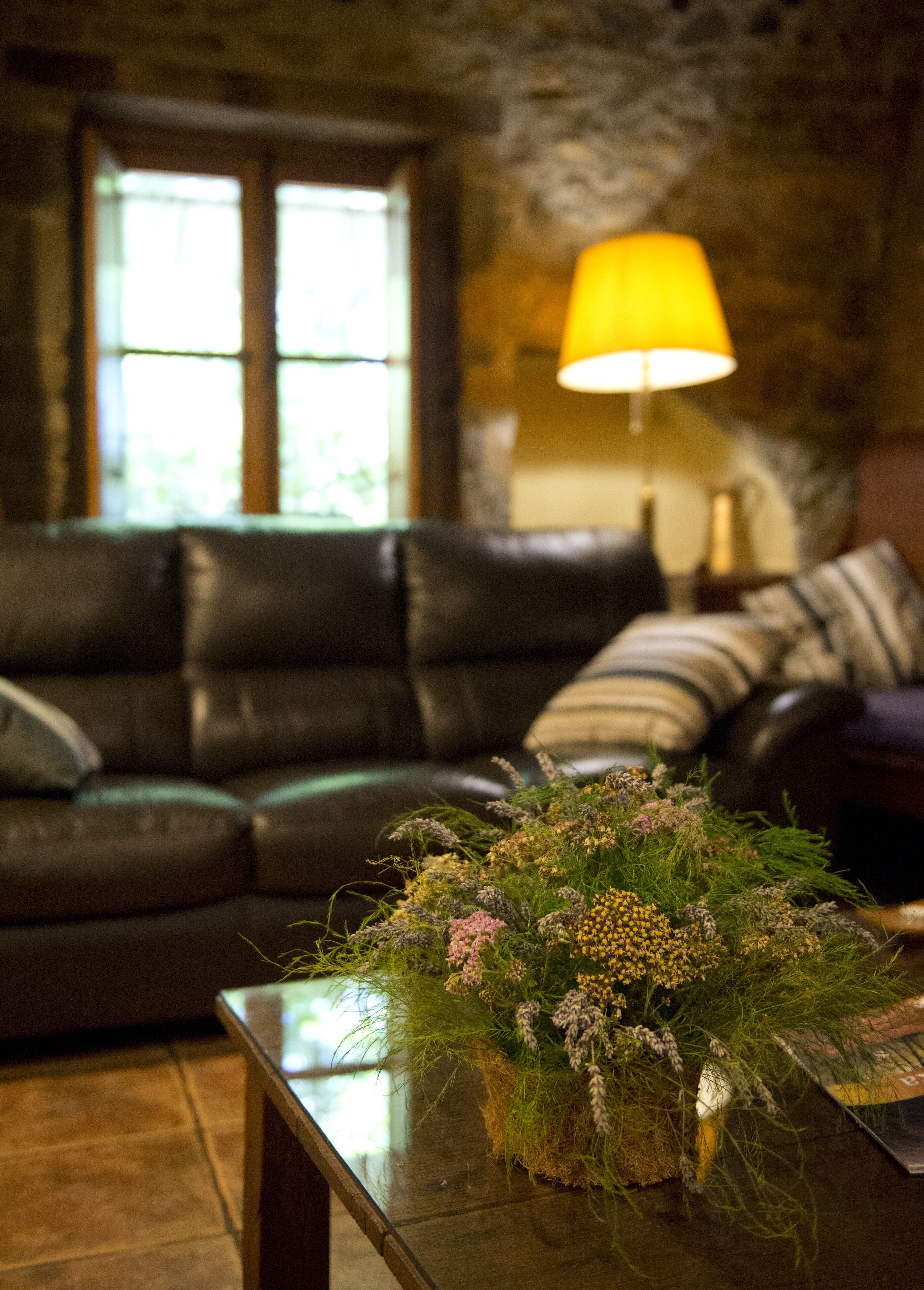A living room with a dark leather sofa, a wooden coffee table with a floral arrangement, and a lamp with a yellow shade.