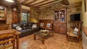 Un salon de style rustique avec un mur en pierre, des meubles en bois, un canapé en cuir et un téléviseur.