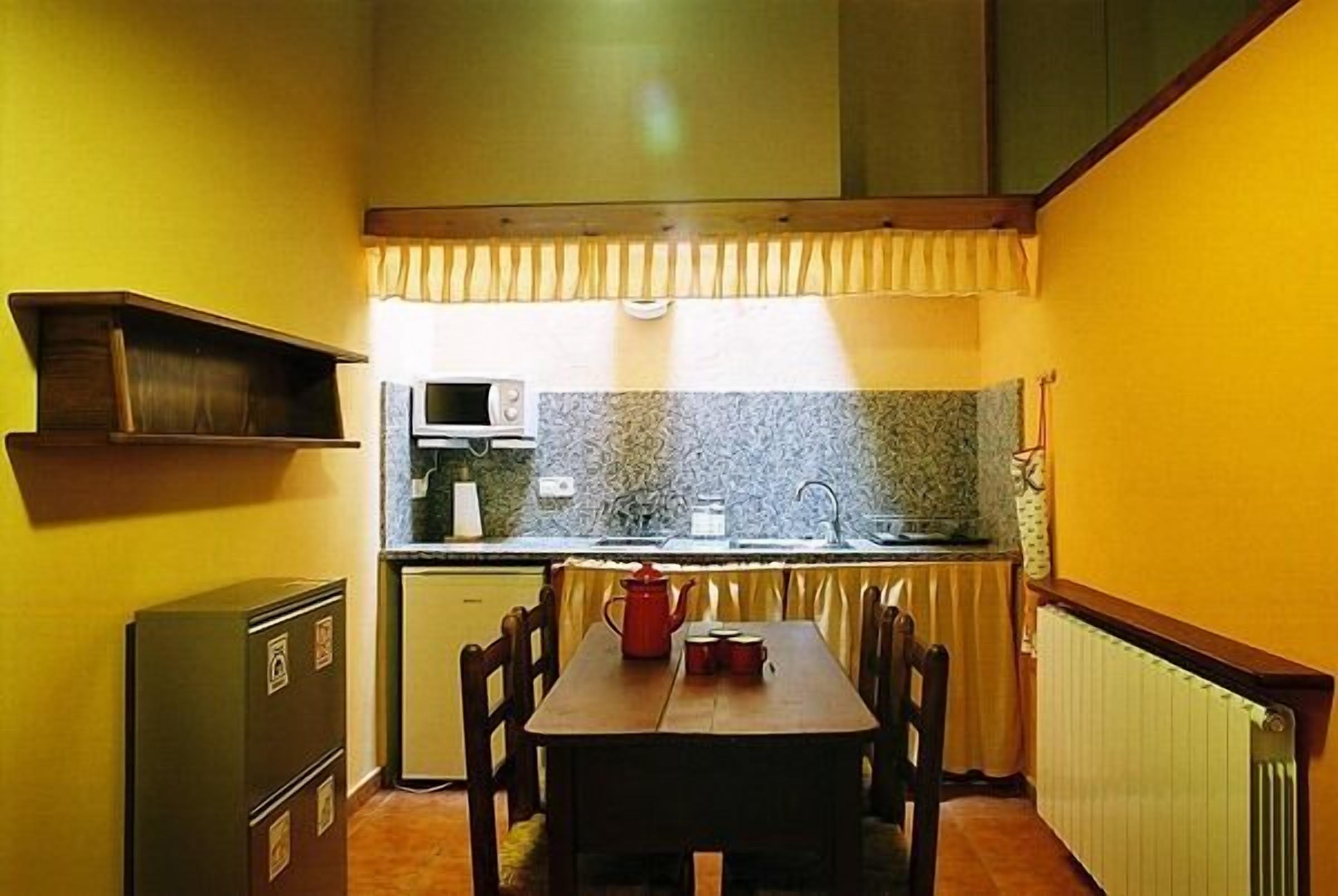 Uma cozinha compacta com mesa de jantar, cadeiras, micro-ondas e geladeira.