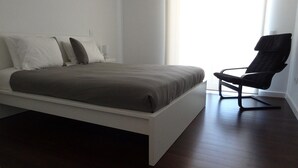 A modern bedroom with a bed, a chair, and a window. - Affordable Luxury Beach Apartment with superb sea view 10 minutes from Porto (Vila Nova de Gaia)