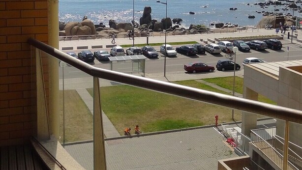 A balcony with a view of the ocean, parking lot, and a grassy area. - Affordable Luxury Beach Apartment with superb sea view 10 minutes from Porto (Vila Nova de Gaia)