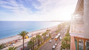 Una carretera costanera amb una platja i palmeres, un autobús i un edifici amb un balcó.
