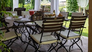 Eine Terrasse im Freien mit Tisch und Stühlen, umgeben von Pflanzen und einem Pergola.