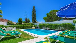 Una piscina con sillas de descanso verdes y un paraguas azul.