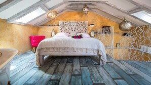 A bedroom with a sloped ceiling, a bed with a decorative headboard, a pink chair, and a white bathtub. - Nicely decorated Casablanca suite with terrace, Wifi, sauna and bikes ... (Veli Lošinj)