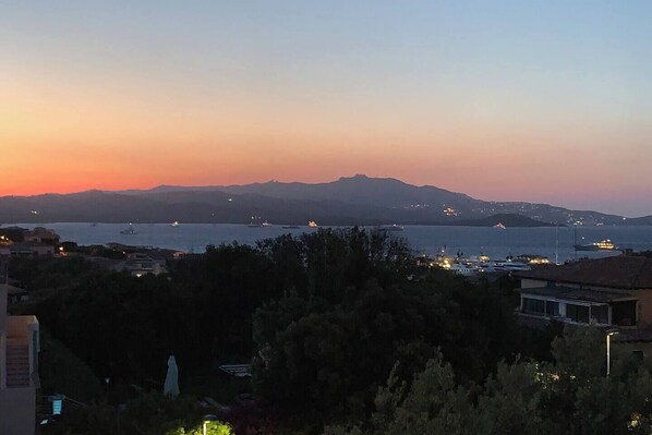 Une vue d’une ville côtière au crépuscule, avec des bateaux sur l’eau et des bâtiments au premier plan.