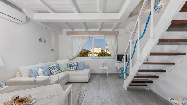 A modern living room with a white sofa, a dining table with a shell centerpiece, a small white table, and a staircase with blue ropes. - To complete (Porto Rotondo)