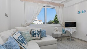 A modern living room with a white sofa, decorative pillows, a small table with a vase, and a TV on a stand. - To complete (Porto Rotondo)