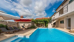 A swimming pool with lounge chairs, a stone wall, and a building with a red roof and balconies. - Villa Torine ZadarVillas (Zapužane)