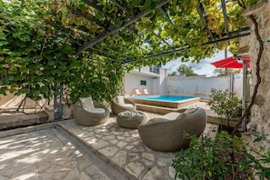 Eine Terrassenfläche mit Steinböden, Korbmöbeln, einem Pool und einer Pergola mit Kletterpflanzen.