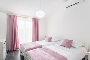 Ein Schlafzimmer mit zwei Betten, einem Fenster mit rosa Vorhängen und einem weißen Deckenventilator.