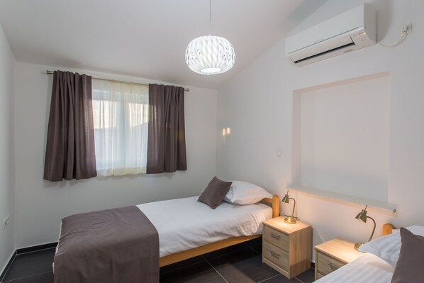 Une chambre à coucher comprenant un lit, des tables de chevet, un luminaire suspendu et un appareil de climatisation.