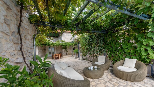 An outdoor seating area with wicker furniture, stone flooring, and a pergola covered with vines. - Villa Torine ZadarVillas (Zapužane)
