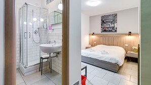 Un bagno moderno con box doccia in vetro, lavabo e specchio. La stanza presenta un letto grande con testiera in legno e un'opera d'arte appesa al muro.