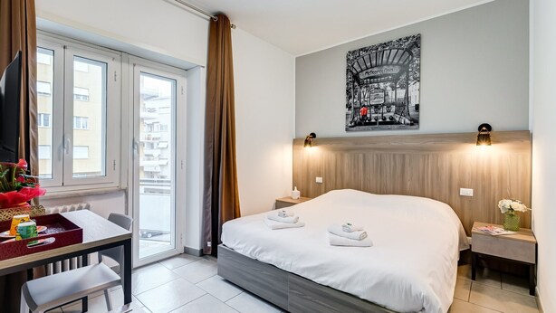 Una camera d'albergo moderna con un letto grande, una scrivania con una sedia, un tavolo da pranzo e vista sulla città dalla finestra.